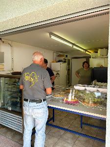 Kuchen steht auf einer Theke, links davon in einem Cooler. Im Vordergrund kauft ein Mann gerade Kuchen.